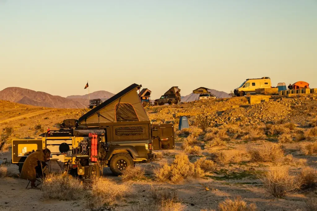 Four-wheel-drive vehicles with rooftop tents camped on open desert ground at sunset in Mojave National Preserve.