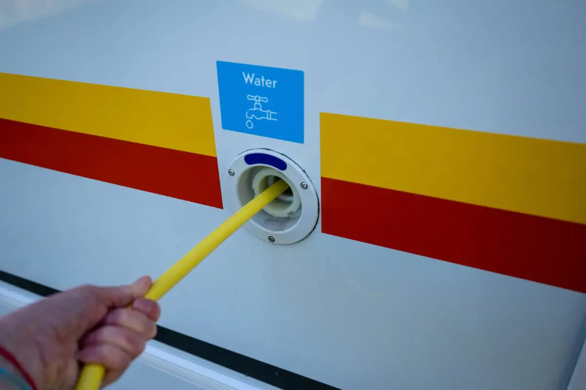 Hand guiding a yellow hose into the fresh water fill inlet on the side of an RV