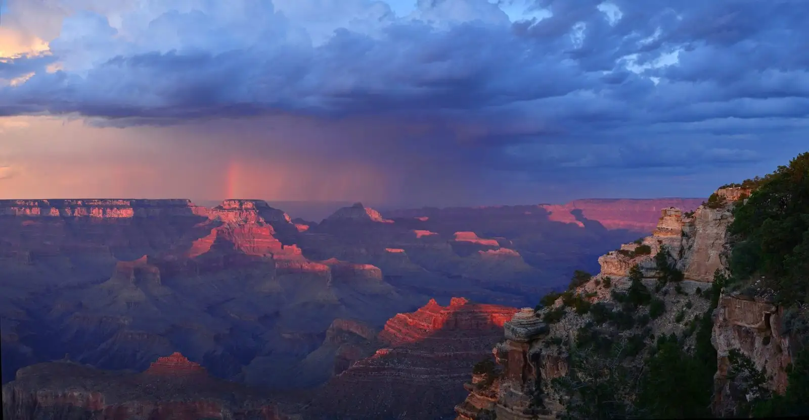 Clouds part over layered Grand Canyon cliffs as sunset casts a red glow from Yaki Point on the South Rim.