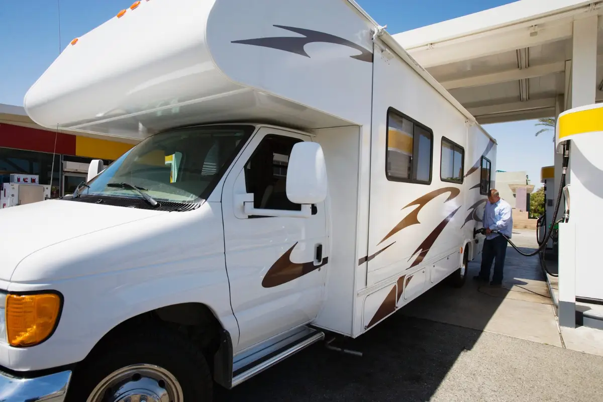 Man refueling a Class C motorhome at a fuel station pump