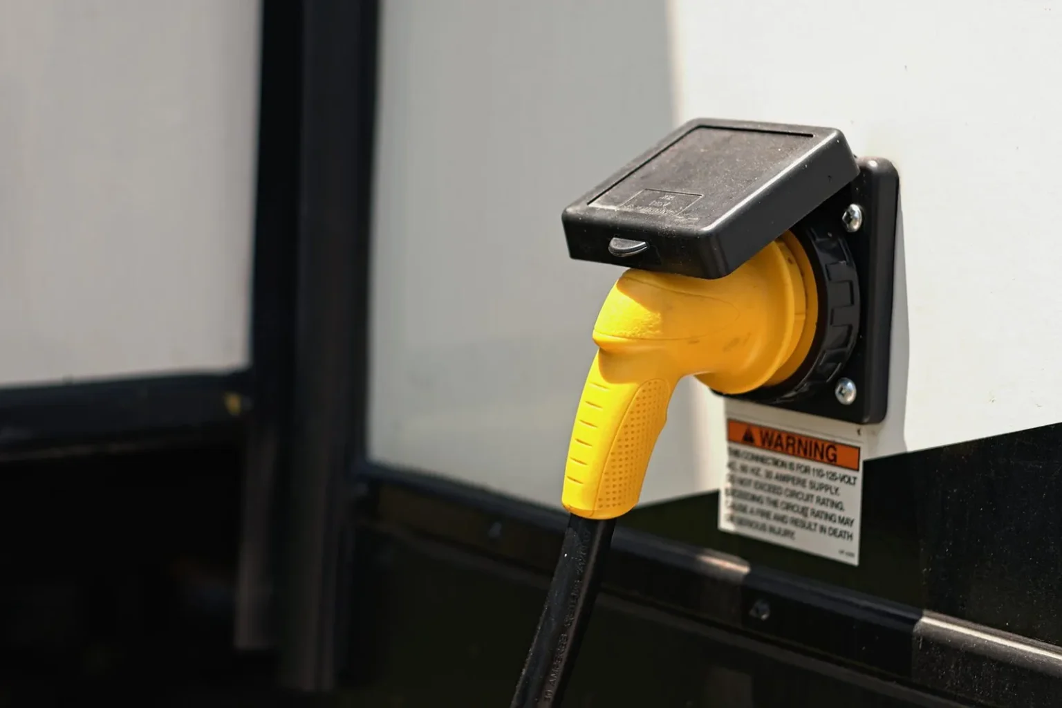 Yellow 30-amp shore power cord plugged into an RV power inlet beside the warning label