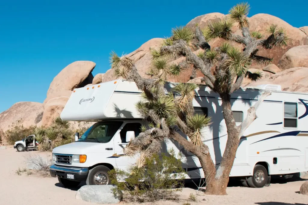 Recreational vehicles parked in dry campsites at Belle Campground, Joshua Tree National Park, among granite boulders and Joshua trees.