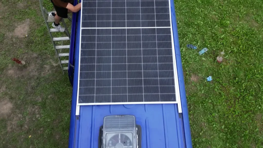 Two installers align a solar panel on the roof of a camper van