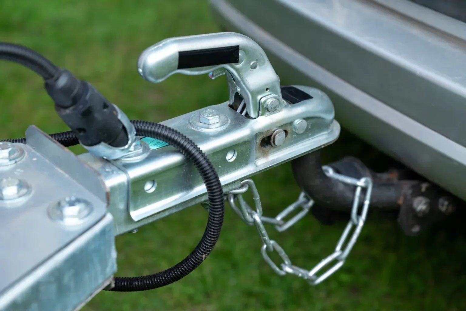 Trailer coupler latched onto the tow ball with safety chains crossed and the 7-way plug connected