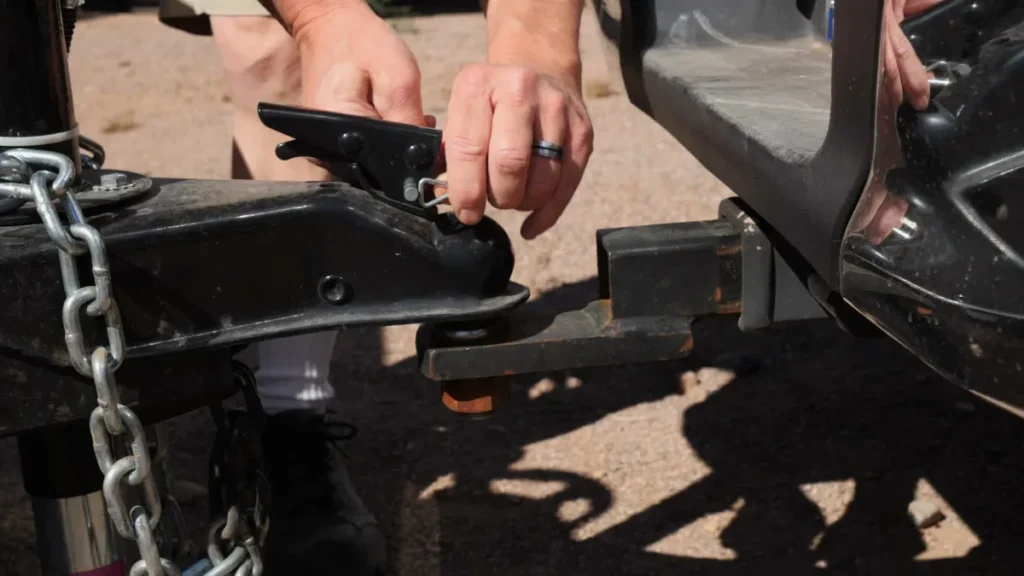 Hands lowering a travel trailer coupler onto the tow ball of a pickup, safety chains hanging below the tongue