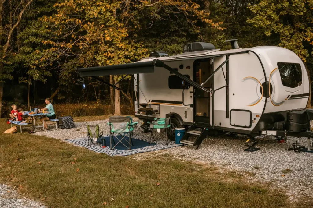Family at a picnic table beside a travel trailer with the awning out on a wooded campsite